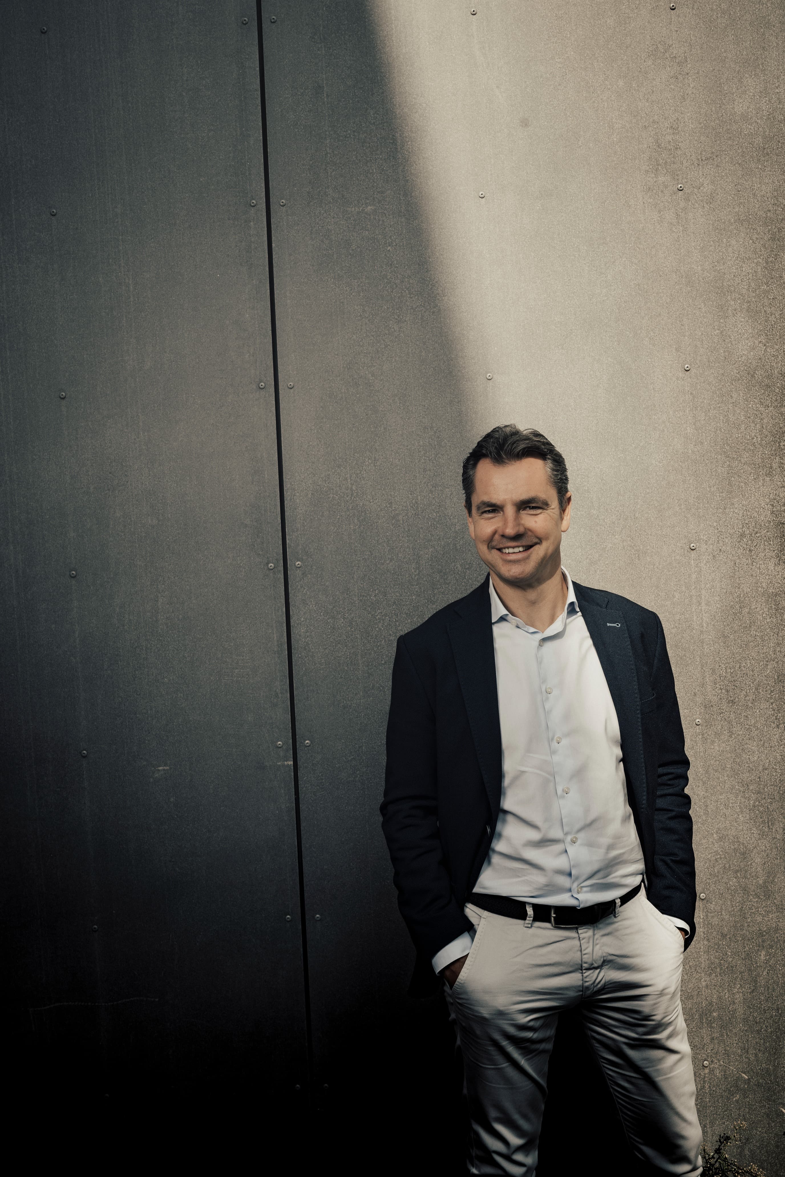 Man staat lachend voor een betonnen muur, half in de schaduw, half in de zon